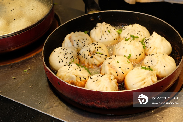 close up white fried buns in a rounded pan under light on cooking bench . Pan-Fried buns stuffed with pork is a popular traditional Chinese food.