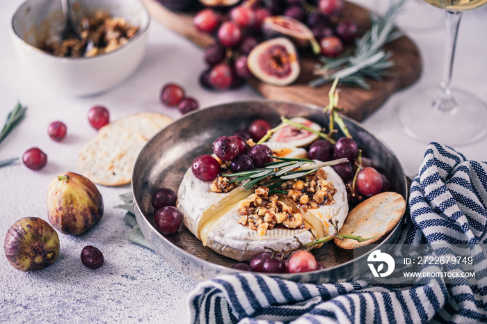 Fancy baked brie cheese platter with honey and walnuts, fresh rosemary. Red grapes, figs and white wine