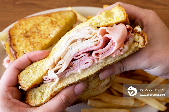 A monte cristo sandwich is being held over a white plate with the other half of the sandwich in view and french fries.