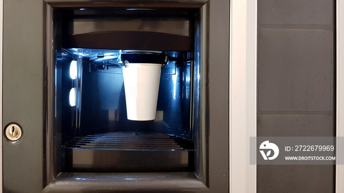 White paper cup in the window of a vending coffee machine. The process of making coffee in a wading machine