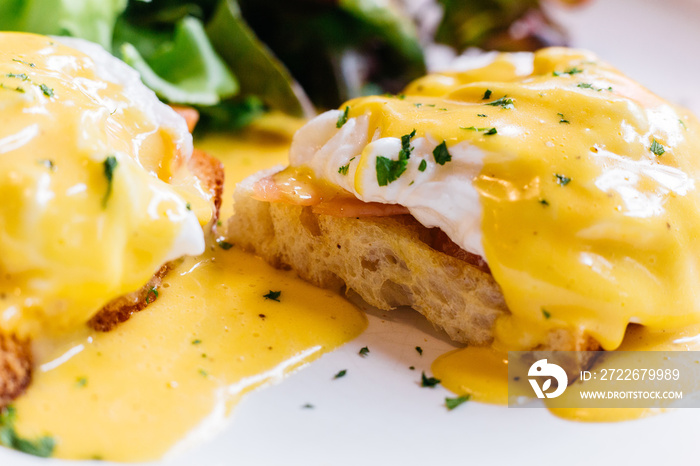 Close up Egg benedict served with salad in white plate on wooden table for delicious breakfast and brunch.