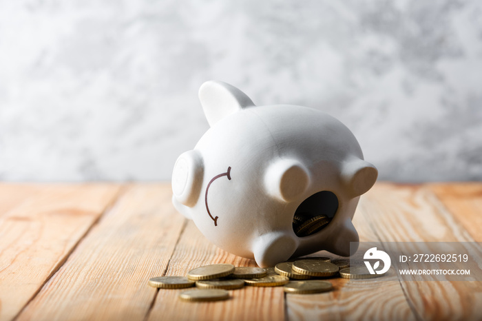 A sad piggy bank behind stack of euro coins symbolizing the fall of monetary assets. White moneybox with golden coins. Crisis concept