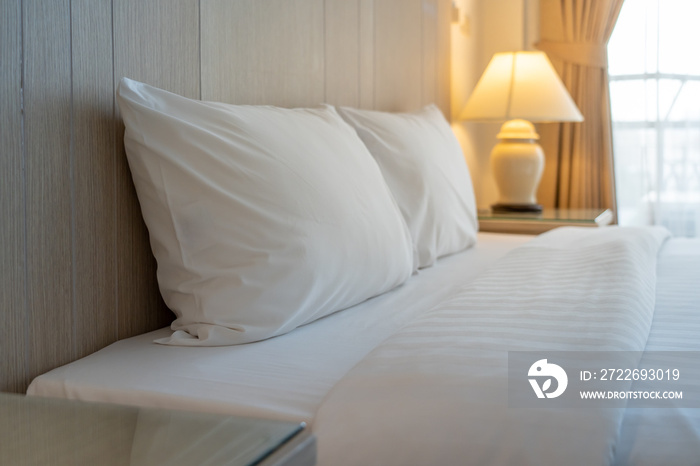 Empty white bed with white pillows and table lamp in a clean bedroom