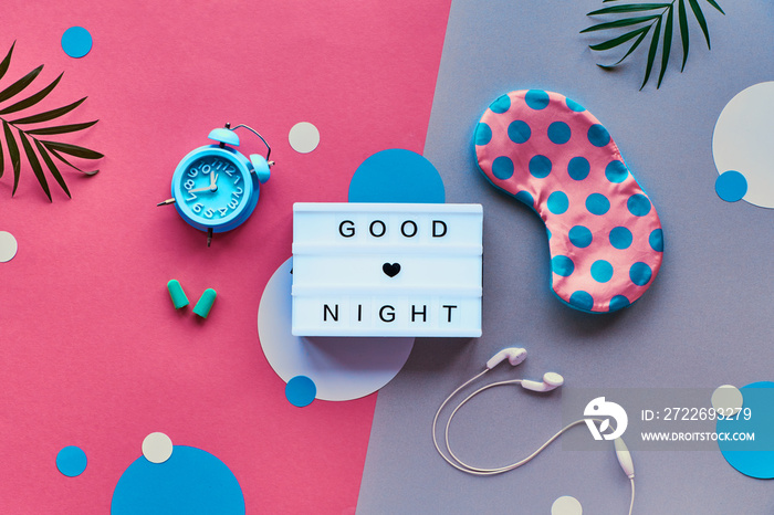 Flat lay, lightbox with text  Good night . Healthy night sleep creative concept. Sleeping mask, blue mint alarm clock, earphones and earplugs. Two tone pink and silver background with paper circles.