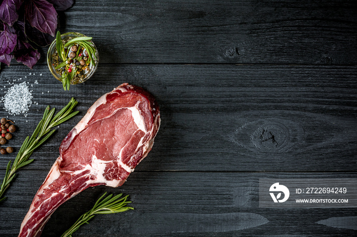 Fresh raw beef with basil and a sprig of rosemary on black wooden background