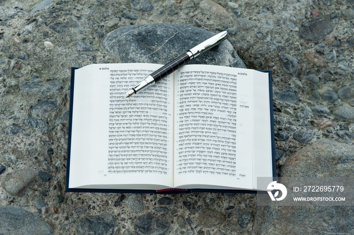 Open Hebrew Bible - TANAKH (Torah, Neviim, Ketuvim - The Law, The Prophets, The Writings) with fountain pen outdoors. Isolated on stones background. Horizontal shot. Close-up.