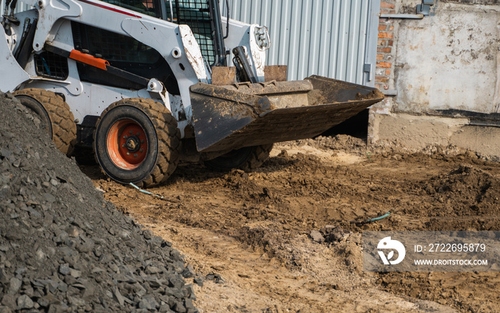 White skid steer loader at a construction site working with a soil. Industrial machinery. Industry.