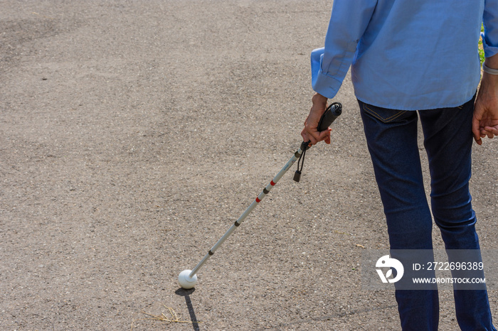 Underfed blind girl with swollen joints and wrists because of arthritis, taking a walk using a white cane on asphalt