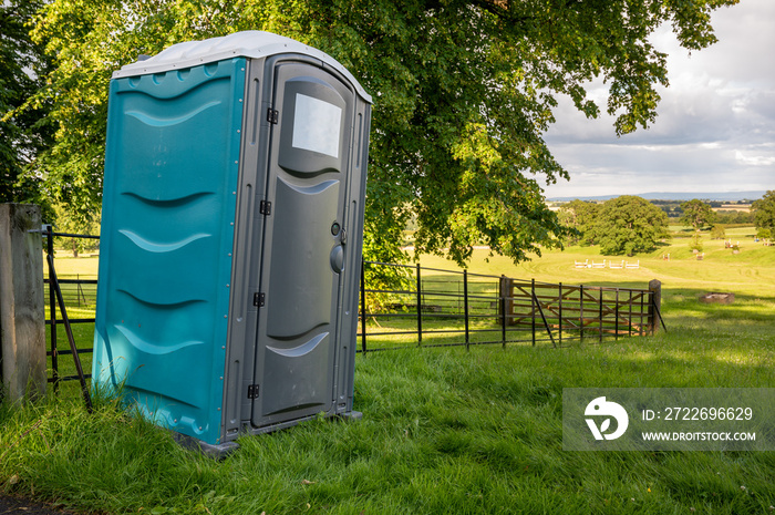 A plastic portable toilet in a field at an outdoor cross country horse trials event