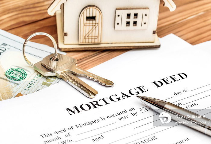 Mortgage deed with keys, money and model of house on the table.