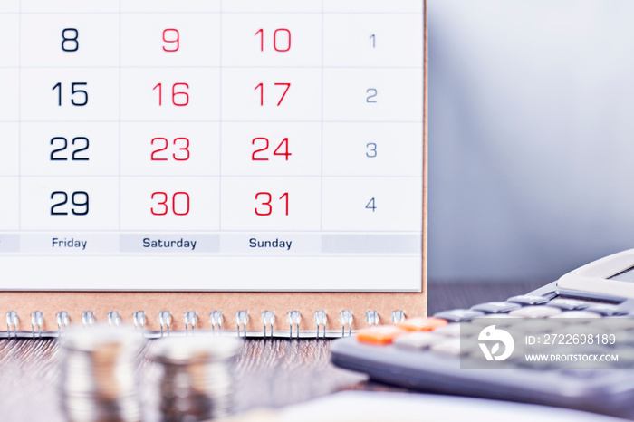 Calendar, calculator and stack of coins in office. Deadline concept. Calendar, coins and calculator on table. Business, finance, taxes, accounting, wages, payroll or money planning concepts