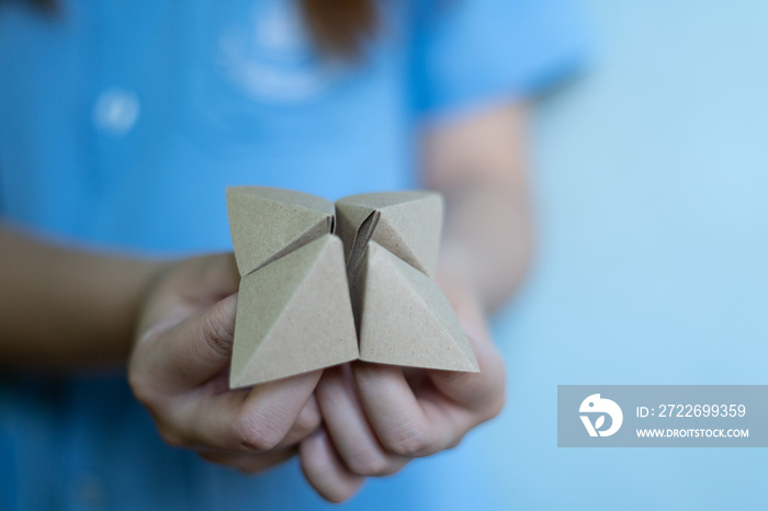 Woman’s hands holding a paper fortune teller on blue background