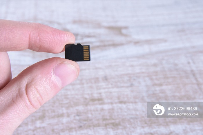 Hand holds flash drive, memory card adapter on wooden background. close up