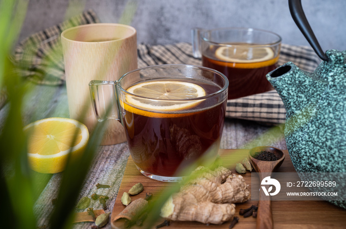 Healthy tea poured into transparent cup. Teapot, lemon, ginger, cardamom, heather bunch and glass jar