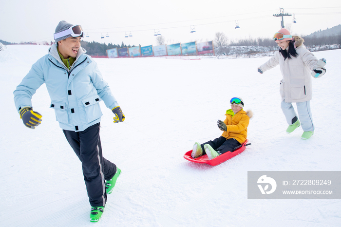 滑雪场上父母和坐在雪上滑板的儿子玩耍