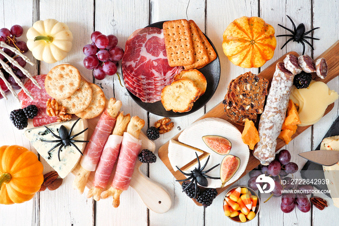 Halloween charcuterie table scene against a white wood background. Selection of cheese and meat appe