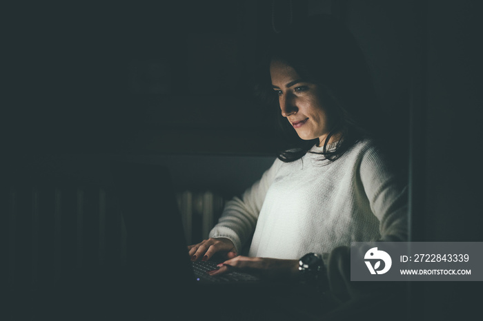 Young woman indoors at home using computer late at night finishing deadline project doing business o