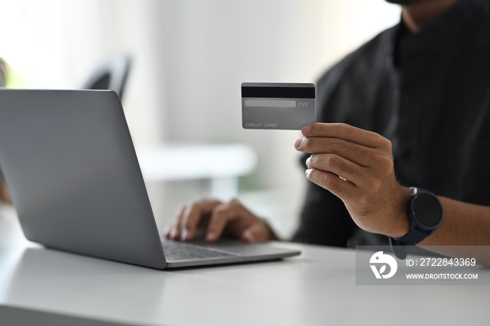 Cropped view of man holding credit card and using laptop for making payment online. Online shopping,