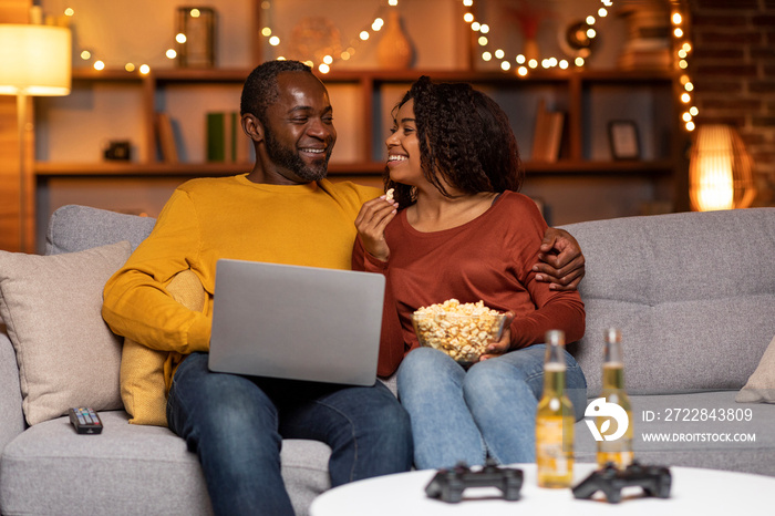 Happily married black couple using laptop at home, watching movie