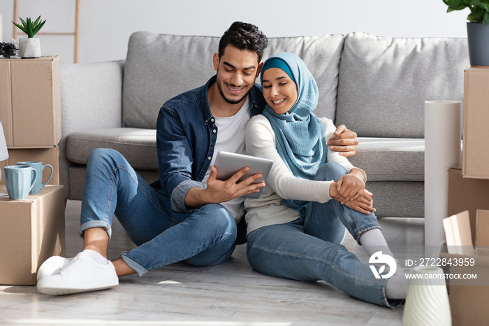 Loving muslim family sitting on floor with tablet among boxes