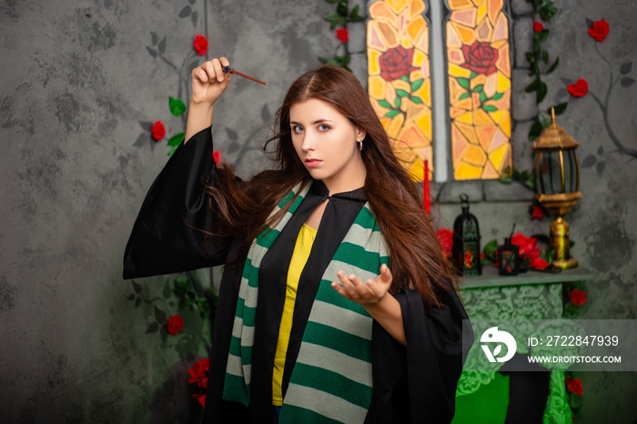 Young woman in a black cloak with a magic wand in her hands, standing against the backdrop of a medi