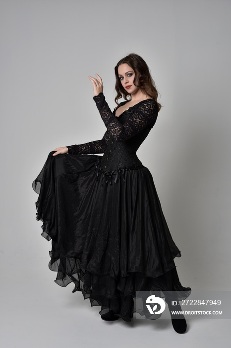 full length portrait of brunette girl wearing long black gown with corset. standing pose on grey stu