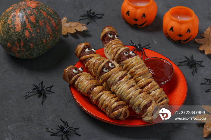 Spooky sausage mummies in dough with ketchup for Halloween party served on dark table