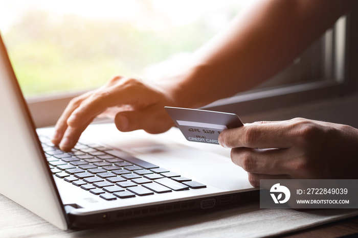 Businessman hand holding credit card with using laptop for online shopping while making orders at ho