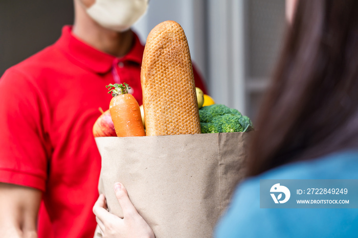 Asian deliver man wearing face mask in red uniform handling bag of food, fruit, vegetable give to fe