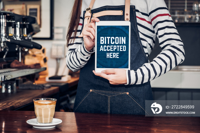 Close up woman barista holding tablet and show bitcoin accepted here on tablet screen at cafe counte