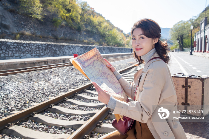 青年女人坐在铁轨旁边看地图