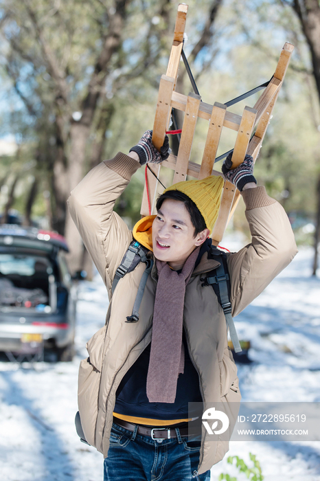 雪地上步行举着雪橇的青年男人