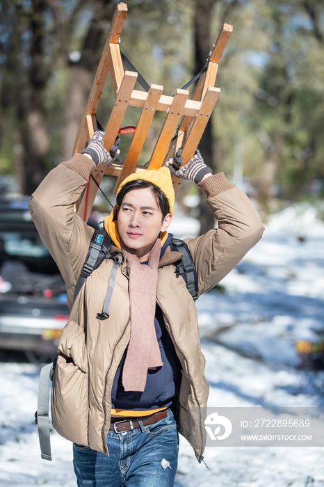 雪地上步行举着雪橇的青年男人