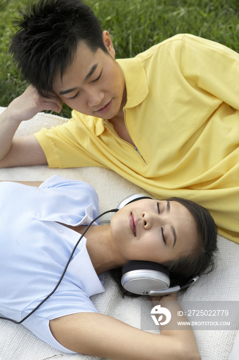 年轻情侣躺在草地上听音乐
