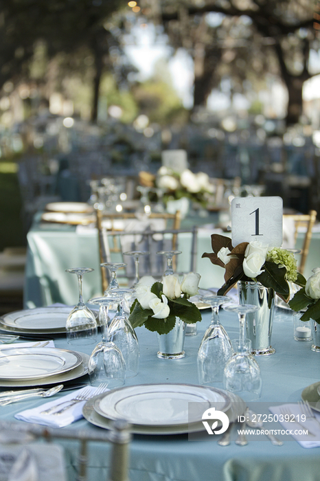 A formal party dining table laid out on a lawn under shady trees 