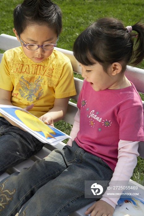 小男孩和小女孩在公园长椅上看卡片