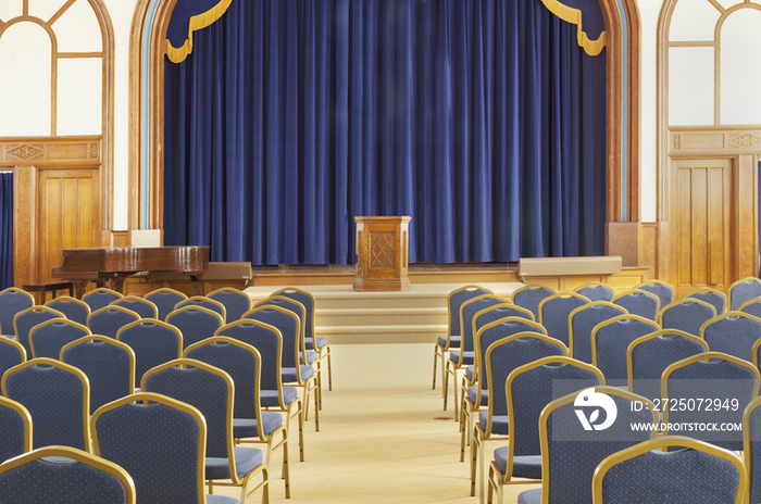 Auditorium with blue chairs, and a stage with curtains