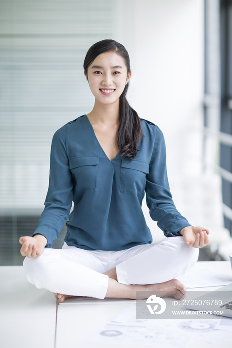 年轻商务女士坐在办公桌上练习瑜伽