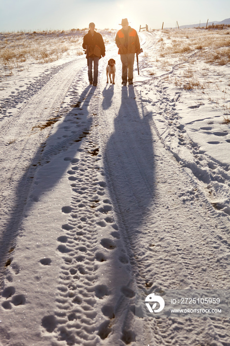 Two hunters walking down snowy trail with dog