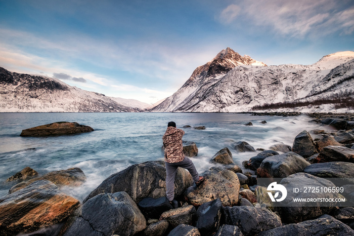 Seascape with snow mountain and photographer standing on rock at coastline