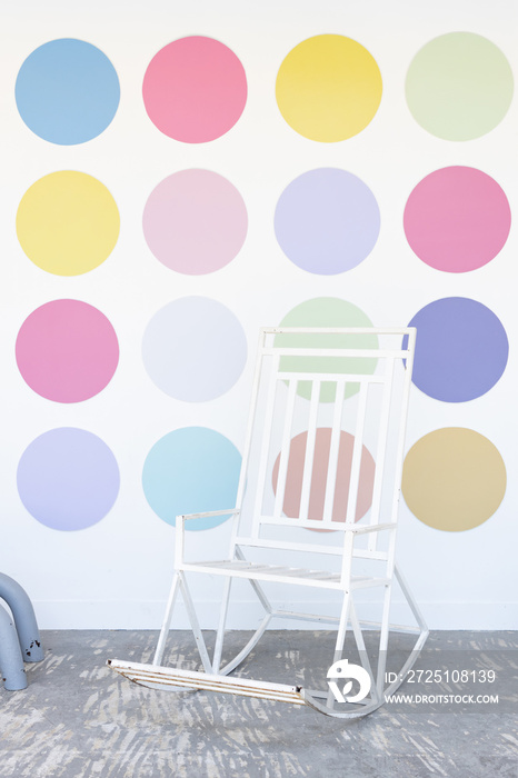 Rocking chair with multicolor circle shape on a white wall background.