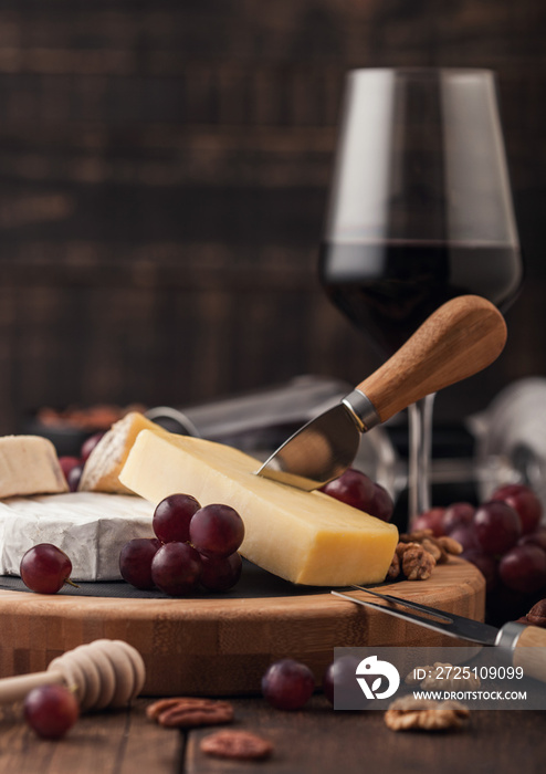 Glass of red wine with selection of various cheese on the board and grapes on wooden background. Blu