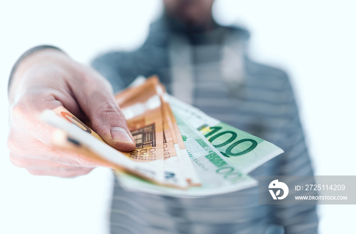 midsection of man holding banknotes in his hand handing it over to someone, paying with cash concept