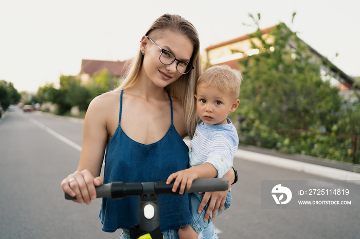 Happy family riding scooter in the neighborhood on the road. Mother and son spend good time together