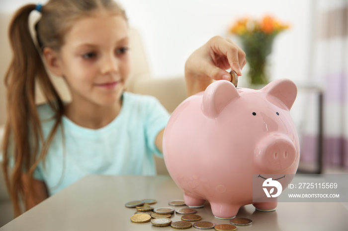 Cute girl putting coins into piggy bank at home