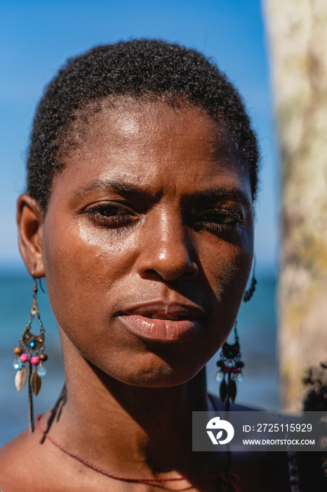 Retrato en primer plano de una mujer africana con cabello corto afro viendo a cámara en un día solea