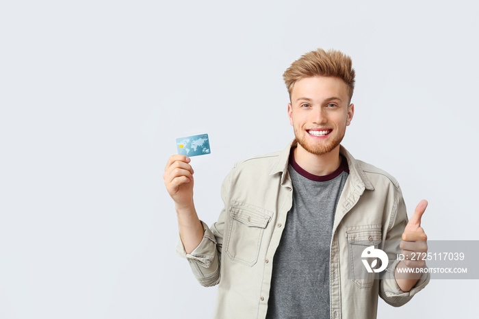 Happy young man with credit card showing thumb-up gesture on white background