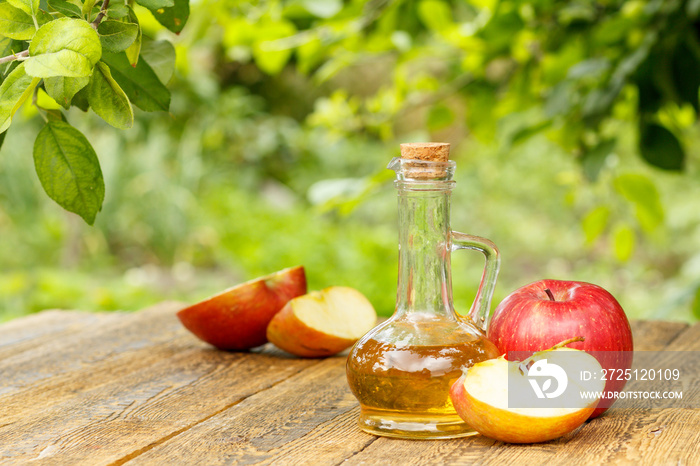 玻璃瓶中的苹果醋和绿色自然背景的木板上的新鲜红苹果