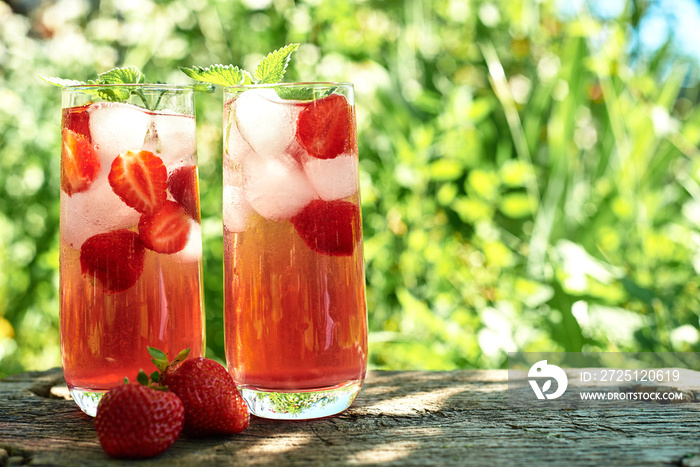 新鲜草莓柠檬水，配冰块和薄荷，放在户外绿色背景的木桌上。