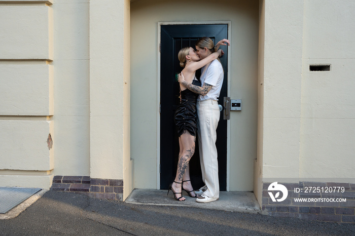 lesbian couple kissing with hands around neck in doorway on street